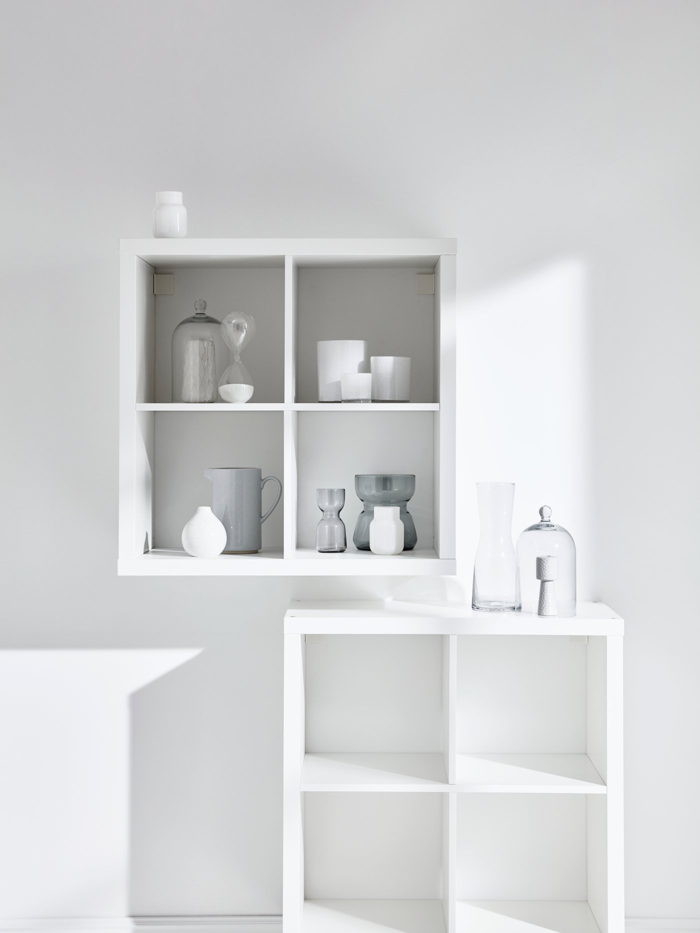 Estantería KALLAX blanca con forma de cubo montada en una pared con jarrones y vasijas. Una unidad idéntica y vacía debajo.