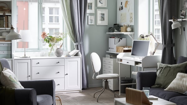 Una sala de un departamento con un sofá y un sillón y un escritorio en una de sus esquinas.