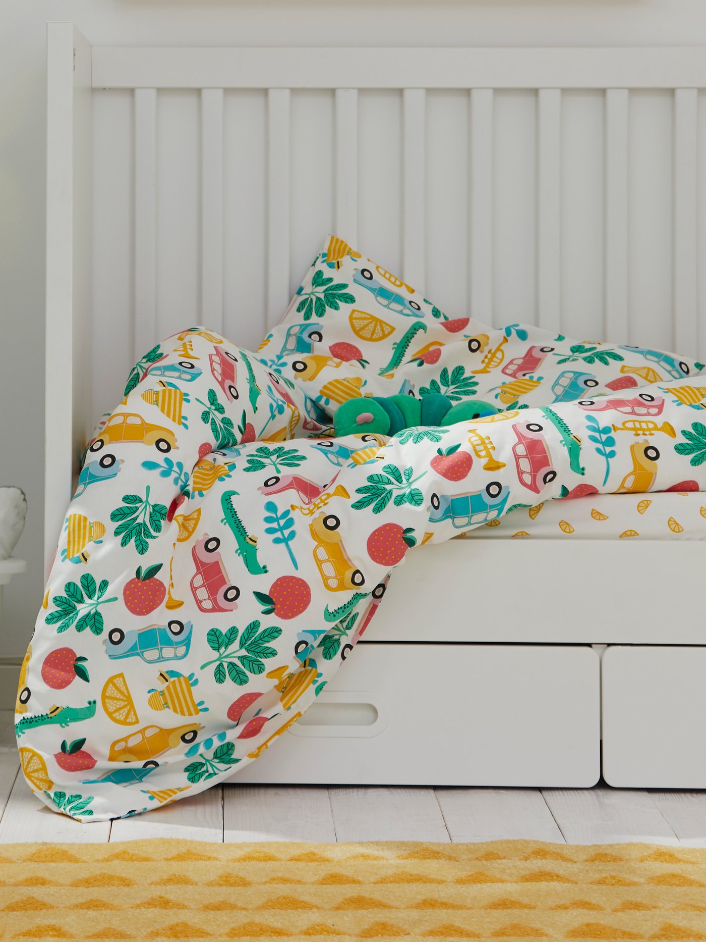 מיטת תינוק STUVA/FRITIDS עם מצעים לחדר השינה RÖRANDE ניצבת מתחת לאחסון לקיר FLISAT ולצד מנורת קיר לד ‏UPPLYST בצבע תכלת.