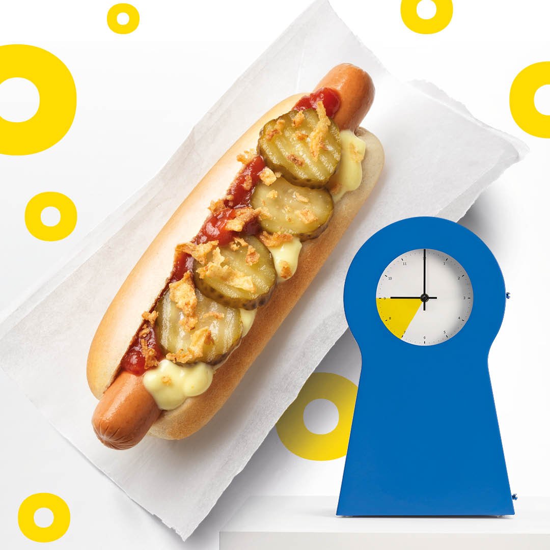 Ein Hot Dog und eine blaue IKEA PS UHR vor einem weißen Hintergrund mit gelben Ringen.