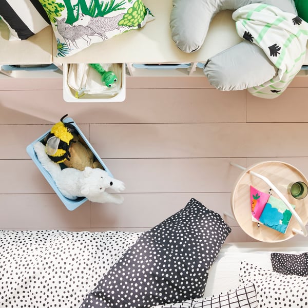 A light blue TROFAST storage box on the floor is filled with plush toys, beside a white TROFAST frame with cushions on top.