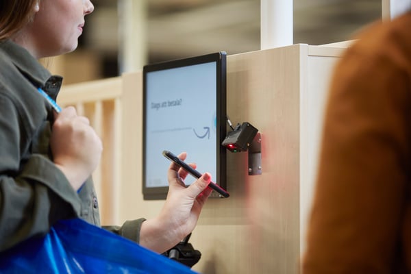 Une femme scanne sa carte IKEA Family numérique à une caisse IKEA.