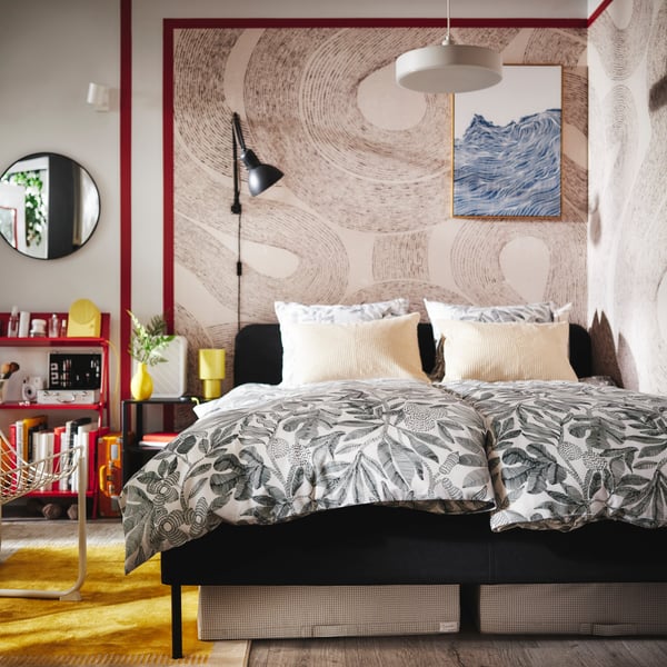 A dark grey SLATTUM upholstered bed in the corner of a bedroom with two duvets covered in BROKDRACENA bed linen.
