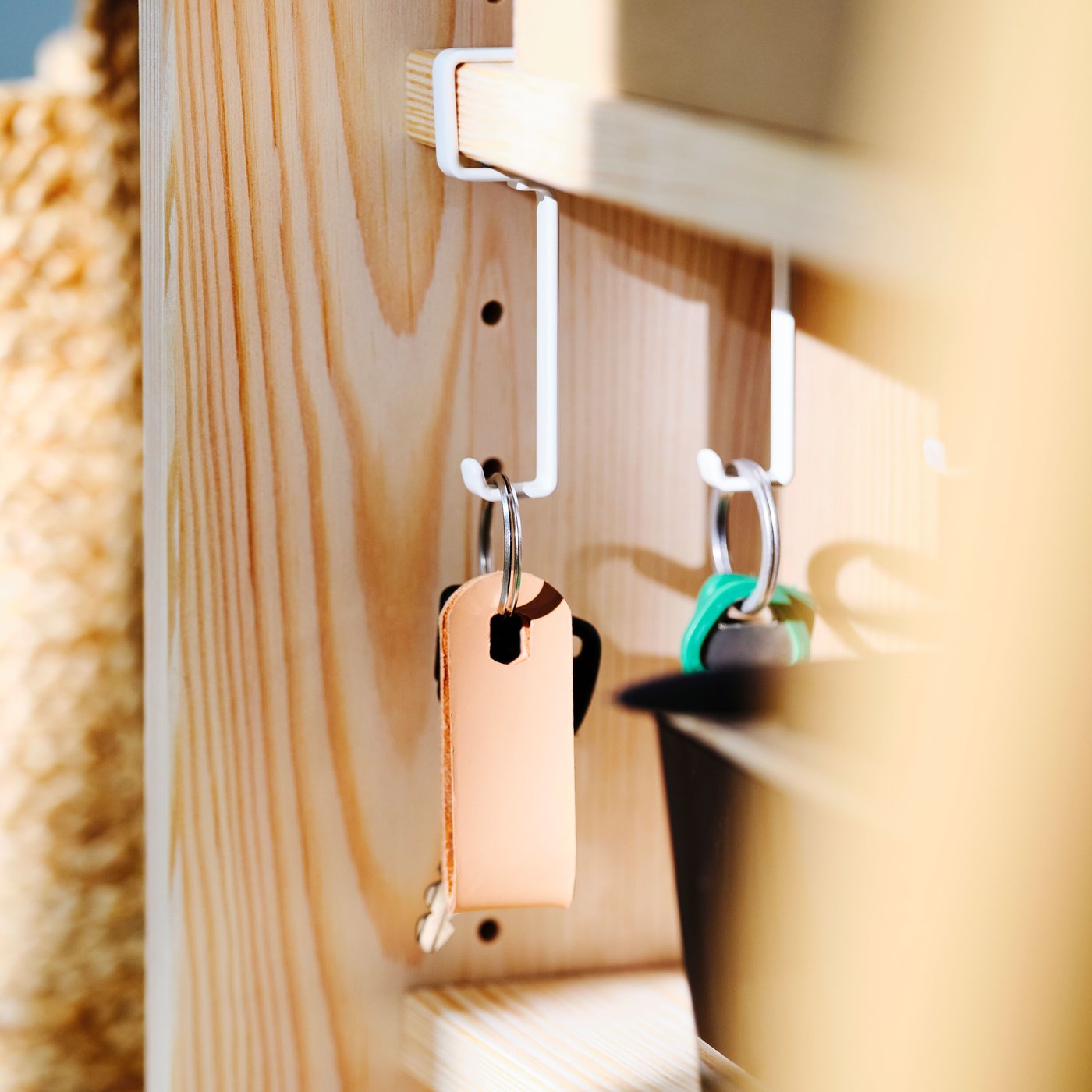 A white PÅLYCKE clip on hook rack on a rail on a wooden shelving unit holding various sets of keys, near a black storage box.