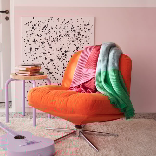 A bedroom features a multicolour MARGOSATRÄD throw placed on a Kelinge orange DYVLINGE swivel easy chair.
