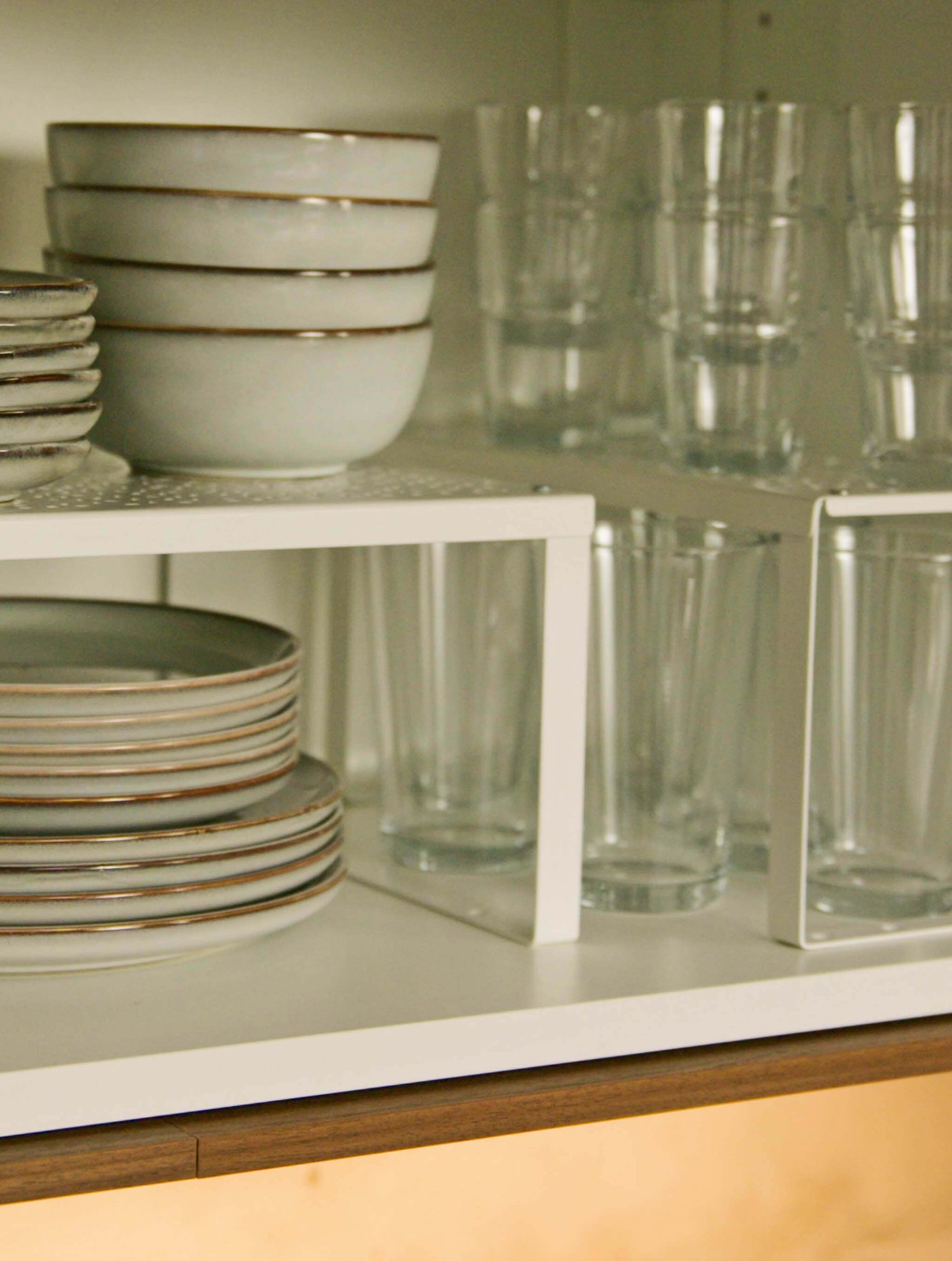 Stacked bowls, plates, and glasses organized neatly on white cabinet shelves.