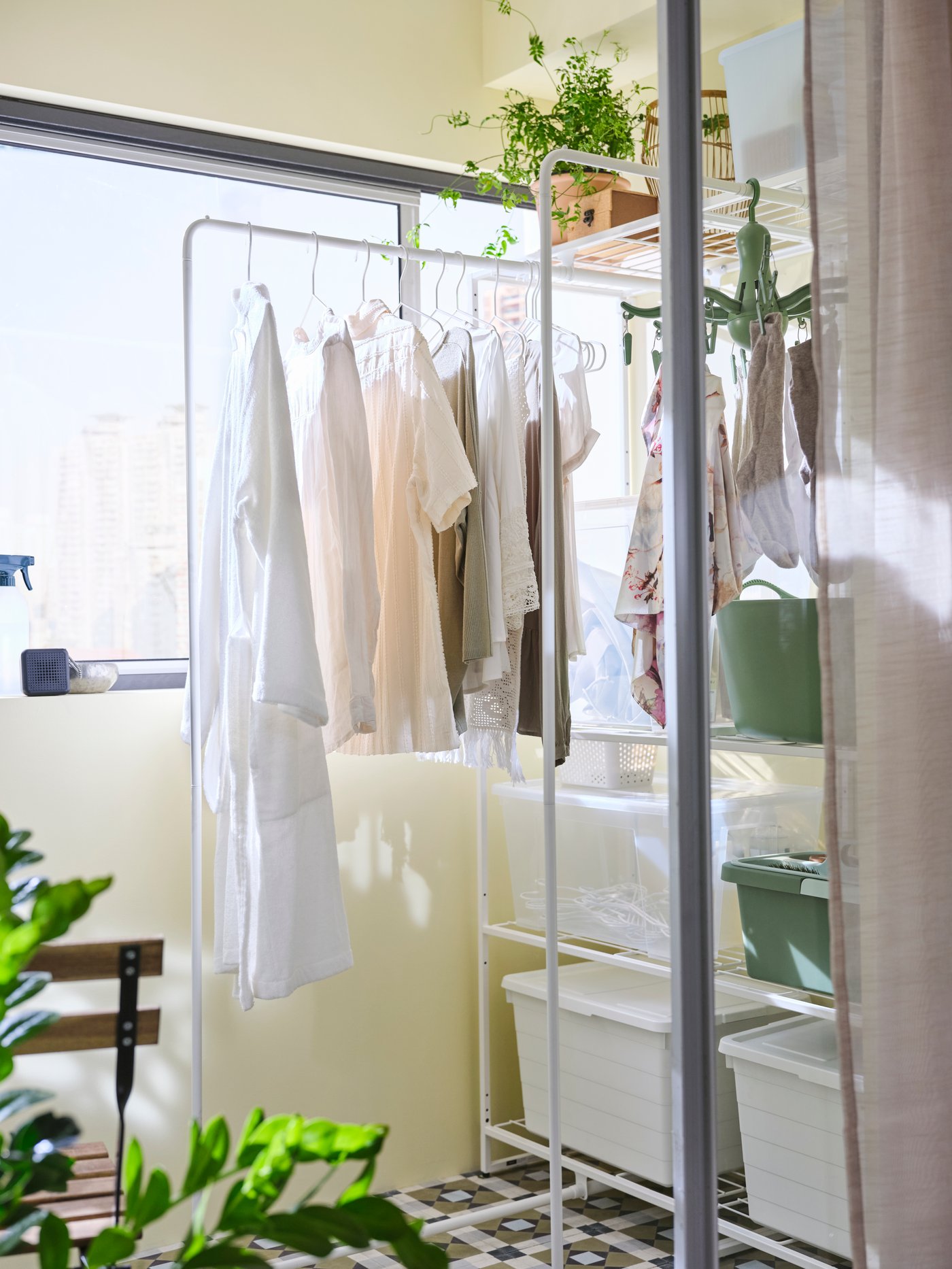 Zwei weiße JOSTEIN-Regale mit Wäscheständern stehen nebeneinander an einer geschlossenen Balkonwand, auf denen die Kleidung liegt.