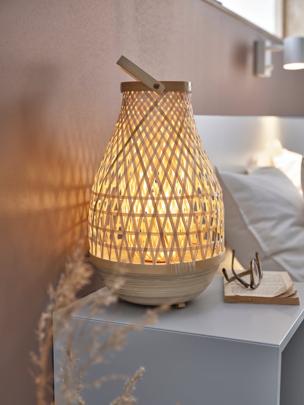 MISTERHULT bamboo table lamp on a bedside table beside a book and spectacles.
