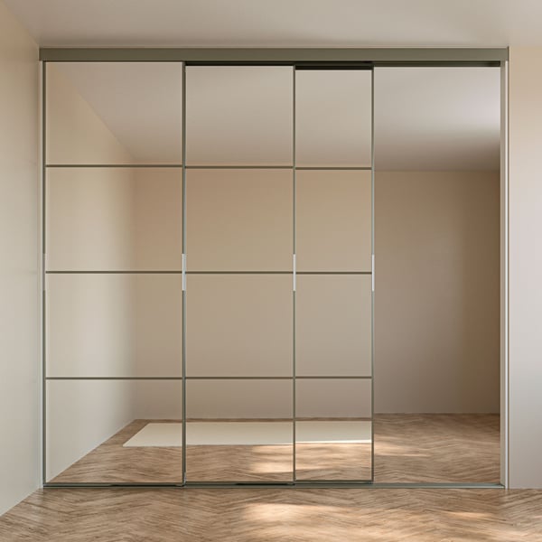 A SKYTTA sliding door solution with high, partly open doors, dividing a bright, unfurnished room with herringbone parquet.