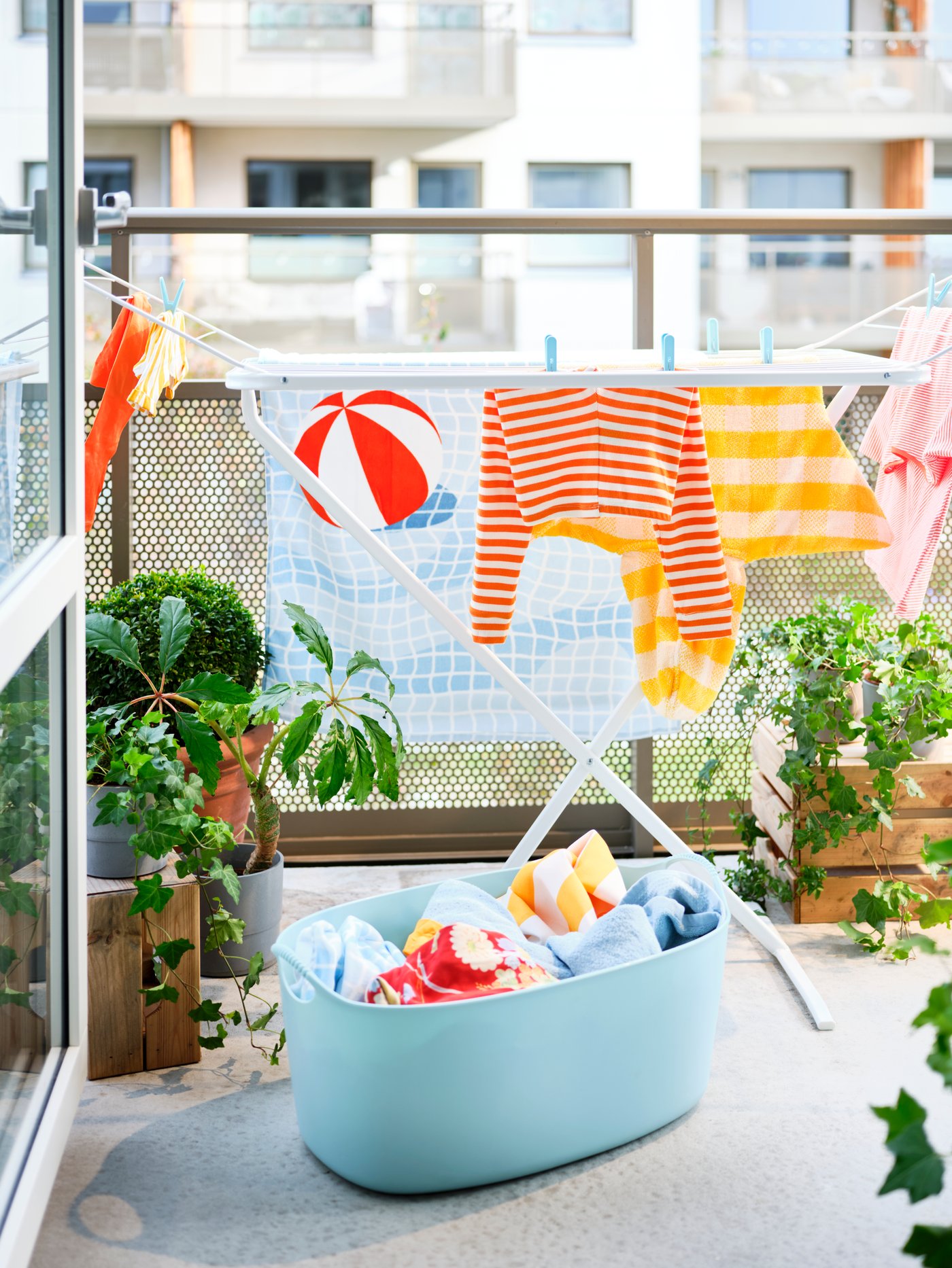 Un tendedero de ropa MULIG con ropa tendida en un pequeño balcón. Frente al tendedero un cesto para la ropa TORKIS.