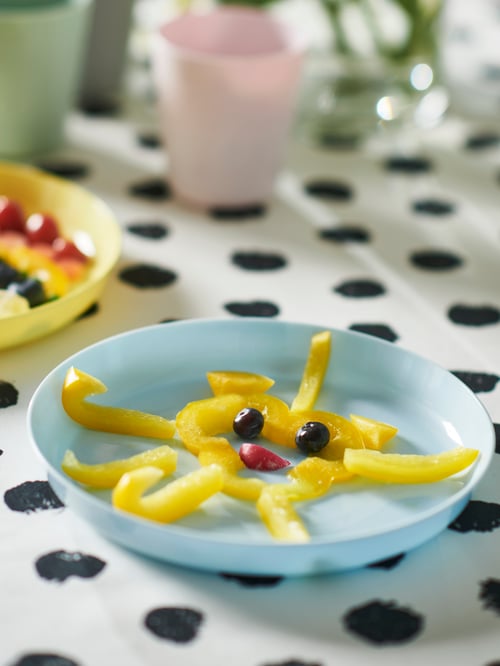 Close-up of a blue plate with yellow food items placed next to a yellow plate, all set on a dotted surface.