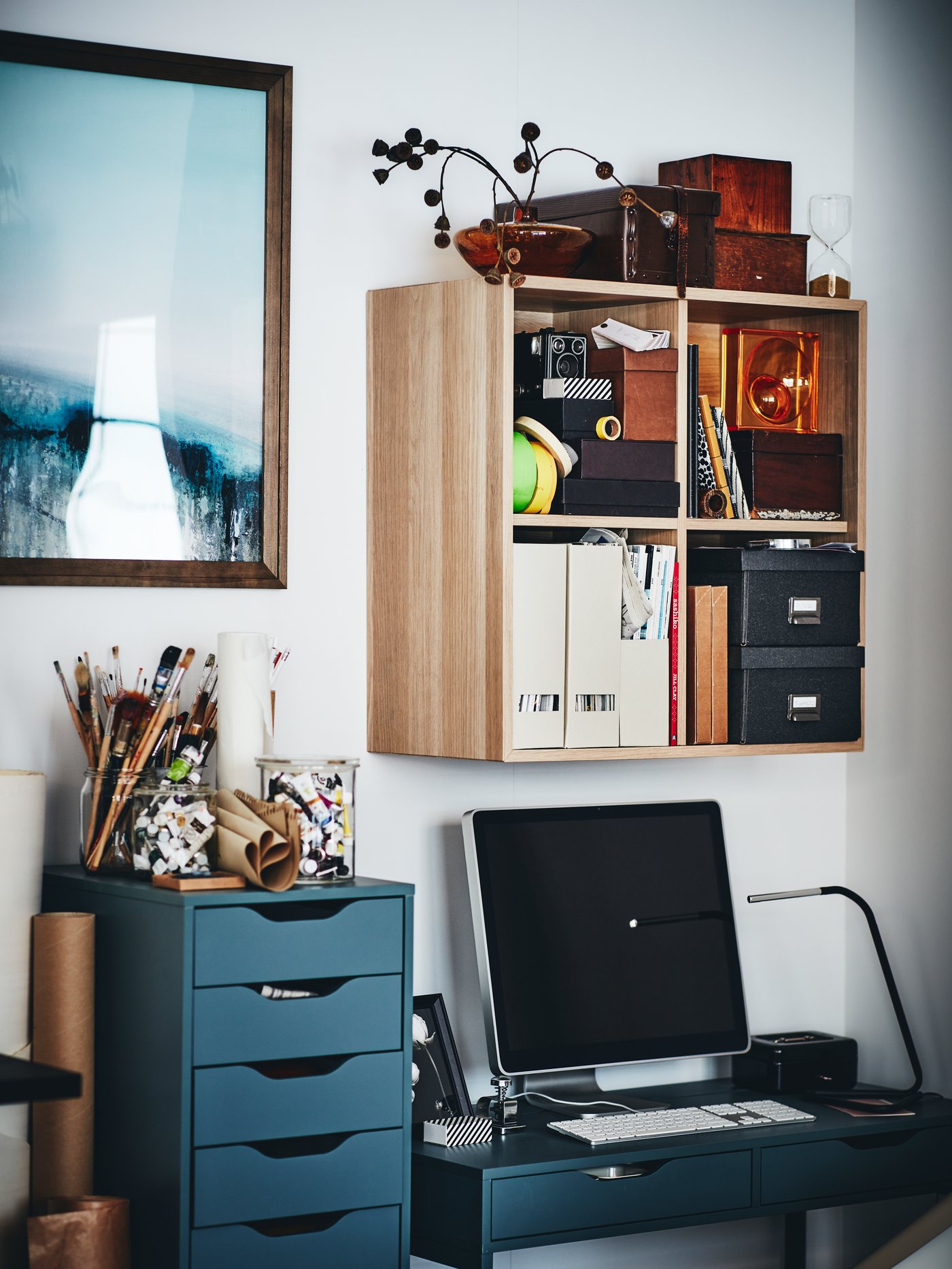 A computer on an ALEX desk in grey-turquoise, next to an ALEX drawer unit, with an EKET wall-mounted shelving unit above.