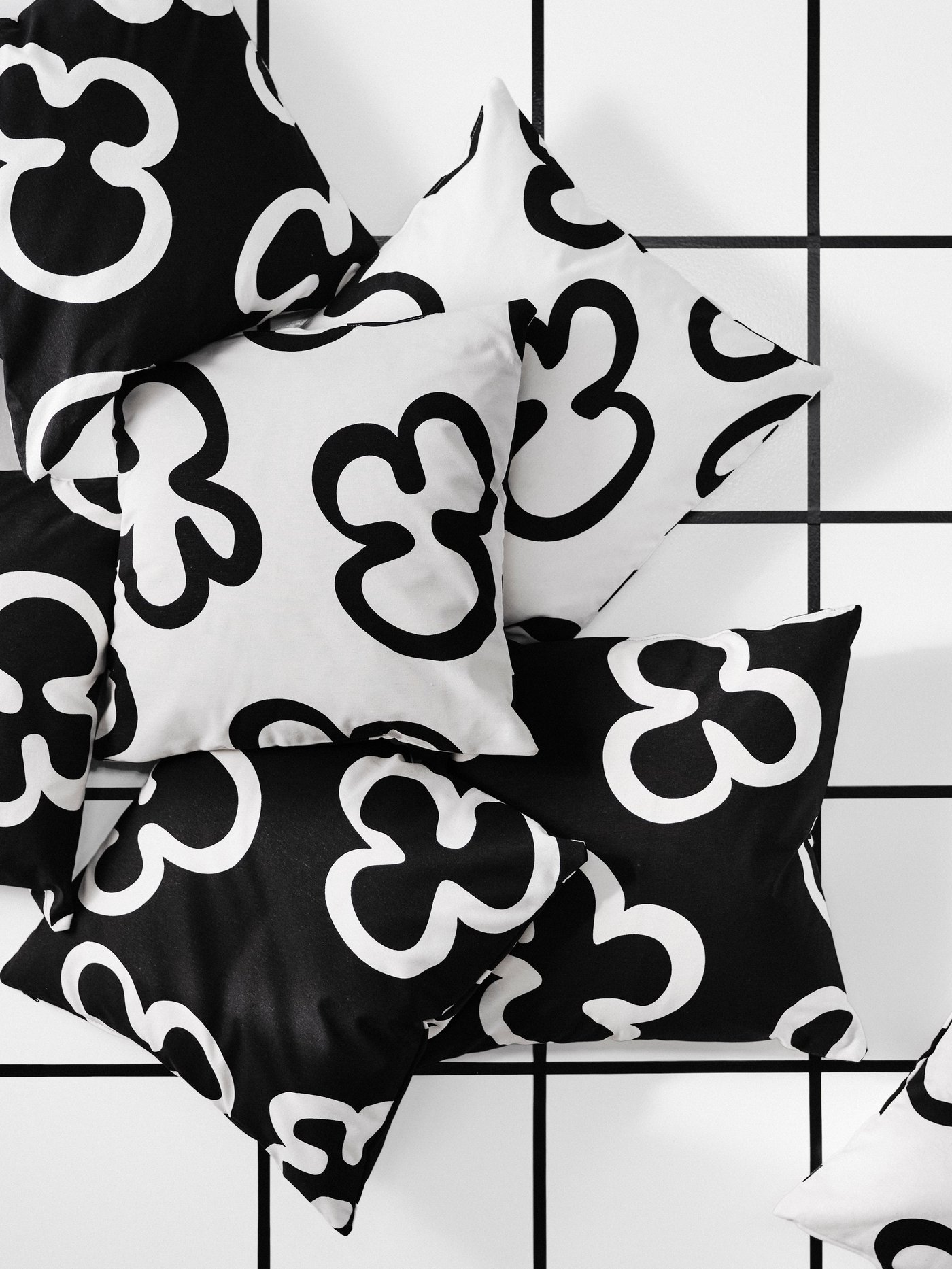 Eight cushions with black and white KLIPPBRÄCKA cushion covers are placed on a floor. The cushions are seen from above.