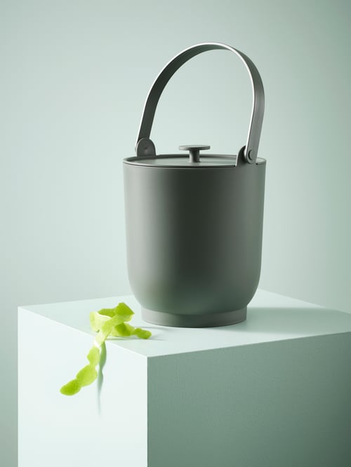 A GREY FARMARKVAST bin with a lid and a handle is placed next to green tape on a square, light-green surface.
