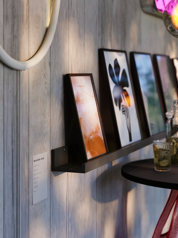 A black wall-mounted MOSSLANDA picture ledge with art in black frames neatly arranged next to a black bar table.
