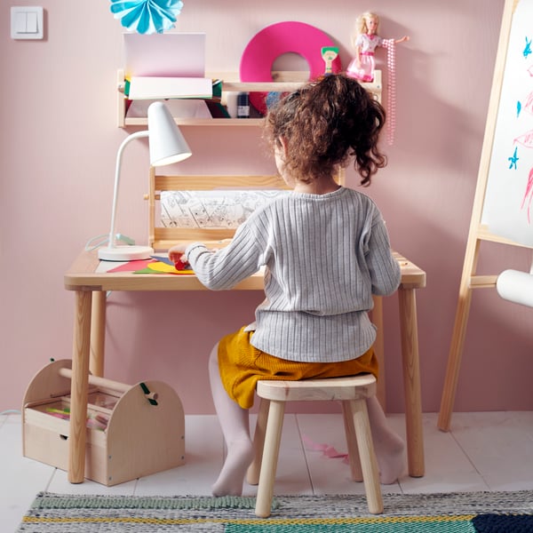 A bright utility room with open units to one side, a woman is sorting laundry on a table and a child is playing alongside.