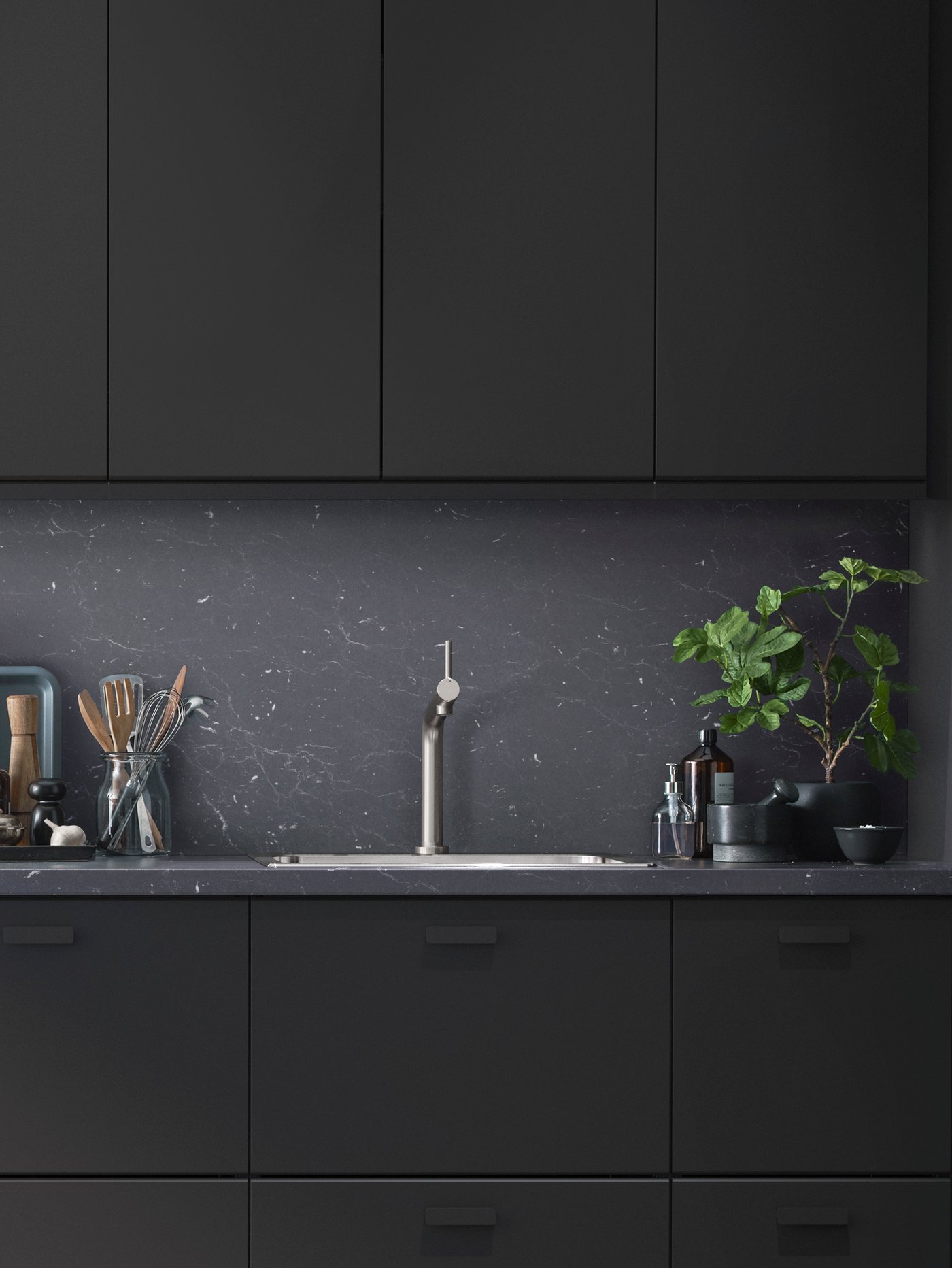 A modern kitchen with black KUNGSBACKA fronts and utensils on one side of the sink and a large plant on the other.