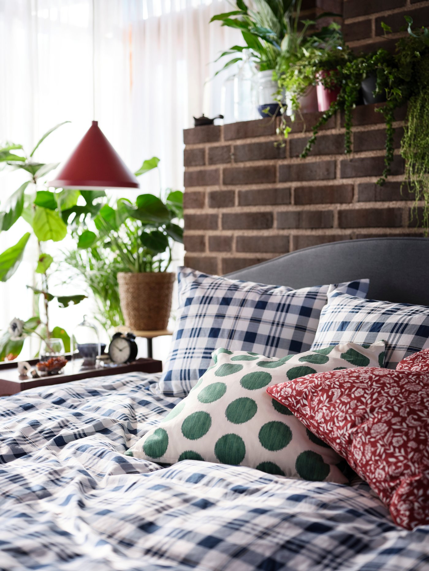 SPIKVALLMO bed linen with white-blue checks, a red-white cushion, a white-green cushion, and green plants in the background.