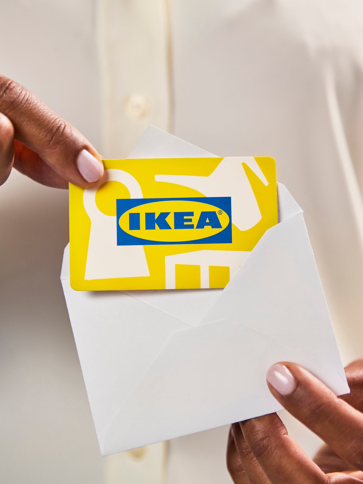 Person placing a yellow IKEA gift card with abstract shapes into a white envelope.