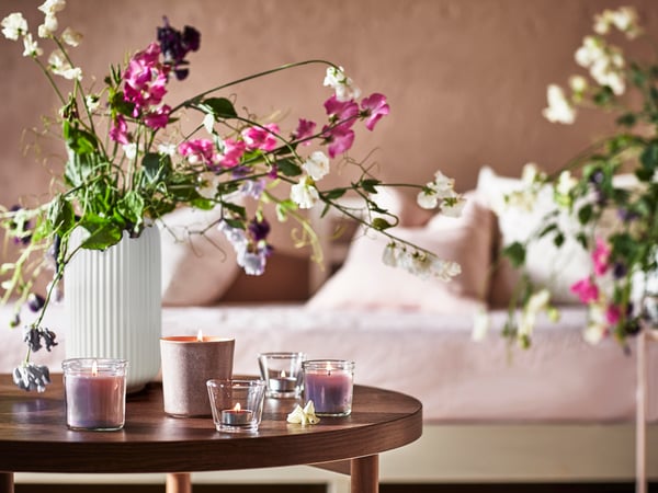 A white vase filled wtih pink flowers sitting with candles on a dark brown stained oak veneer LISTERBY coffee table