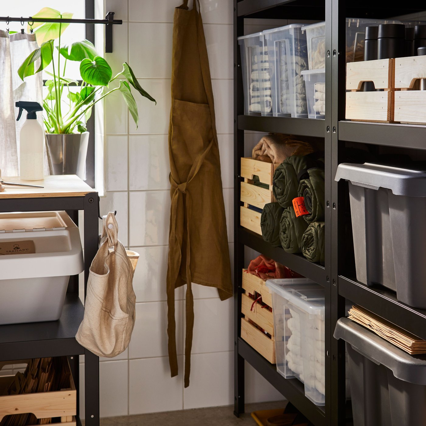 Local de rangement avec des étagères BROR noires posées contre un mur et un établi BROR contre un autre mur, sous une fenêtre.