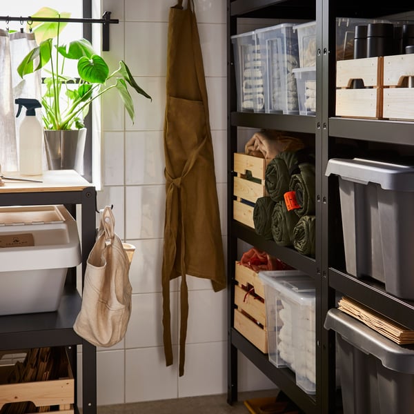 Opbergkamer met zwarte metalen stellingkasten gevuld met plastic bakken, houten kratjes en opgerolde dekens.