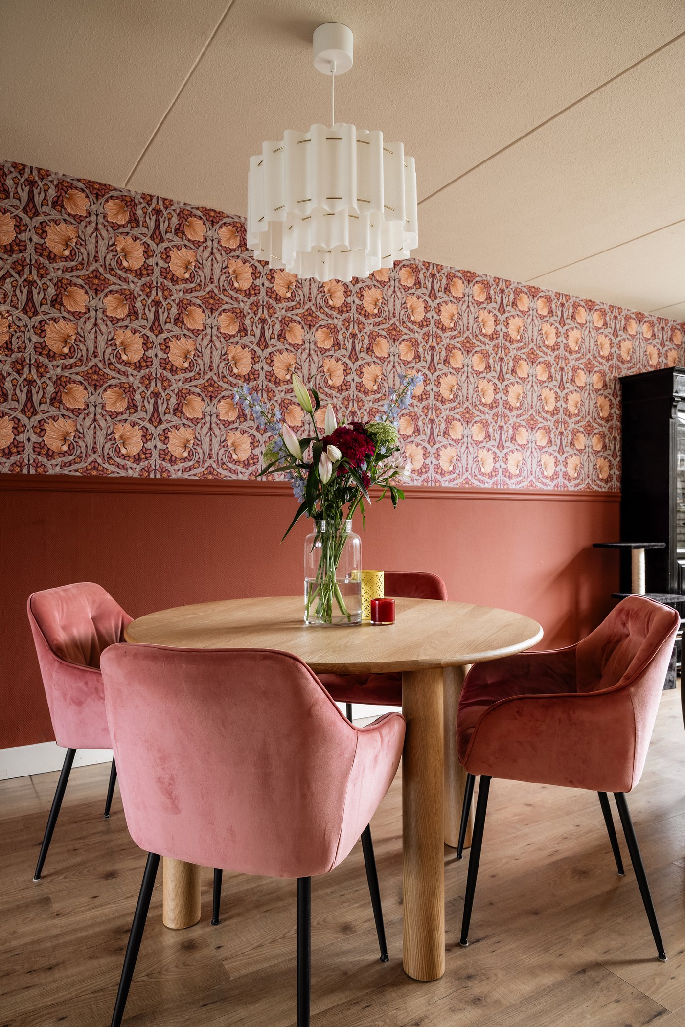Een eetkamerhoek met ronde tafel en vier oudroze kuipstoelen.