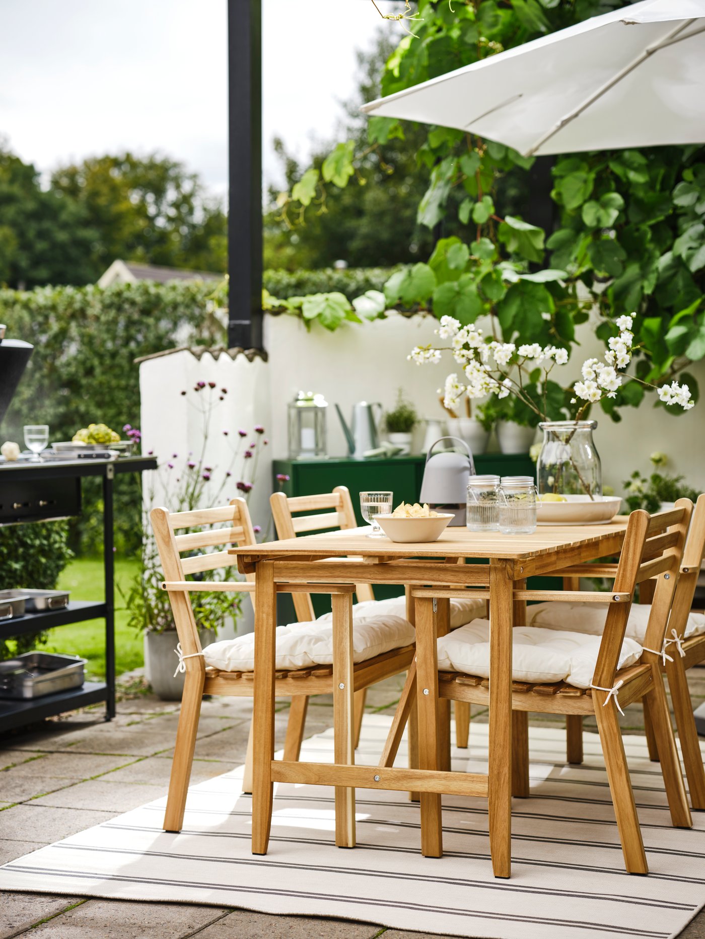 IKEA ASKHOLMEN garden dining table and chairs in acacia wood shaded by a white parasol on a green plant filled terrace