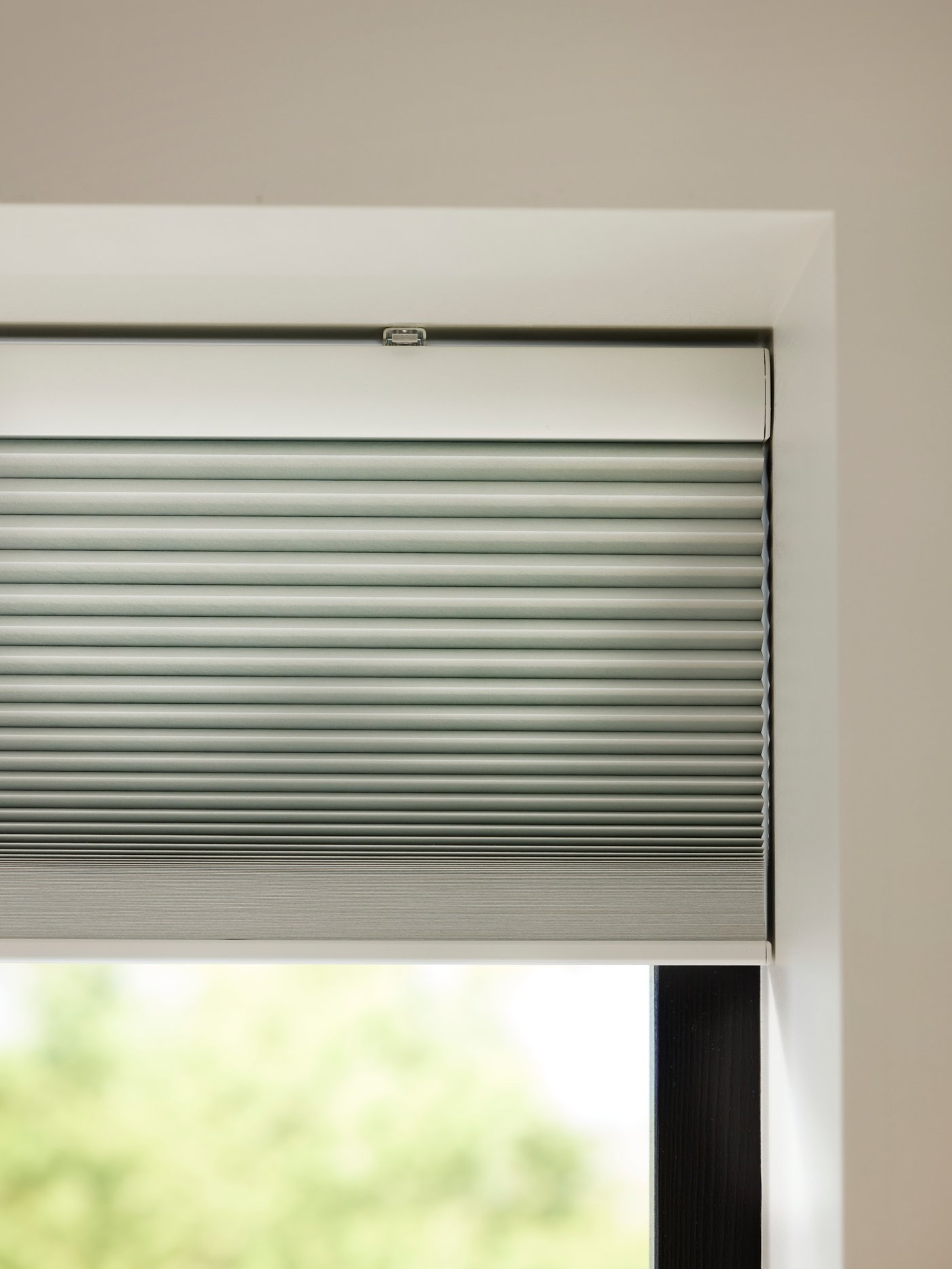 Bovenste hoek van een raam met gedeeltelijk gesloten wit TREDANSEN verduisterend plisségordijn.