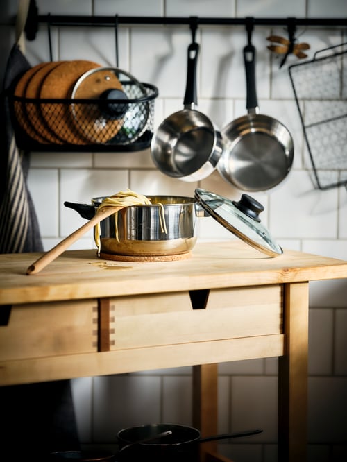 Shot of several items from a cookware set, with a pot with lid on a kitchen trolley, and two other pans hanging in the back.