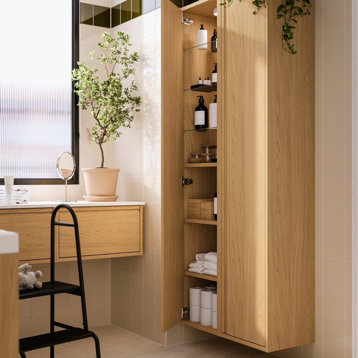 An oak effect ÄNGSJÖN high cabinet has one door open, showing its shelves holding toilet paper rolls, towels and toiletries.