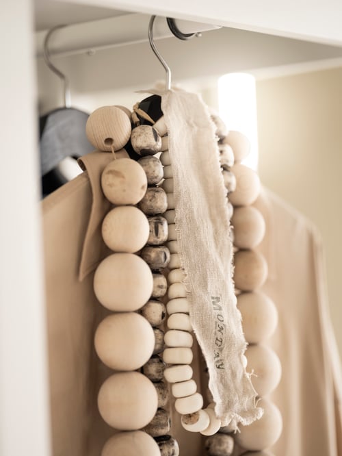 Une salle de bains où se trouvent des cintres en bois noir, des vêtements, des accessoires et, des bijoux. Le tout est sur une tringle blanche à l’intérieur d’un rangement en bois. 