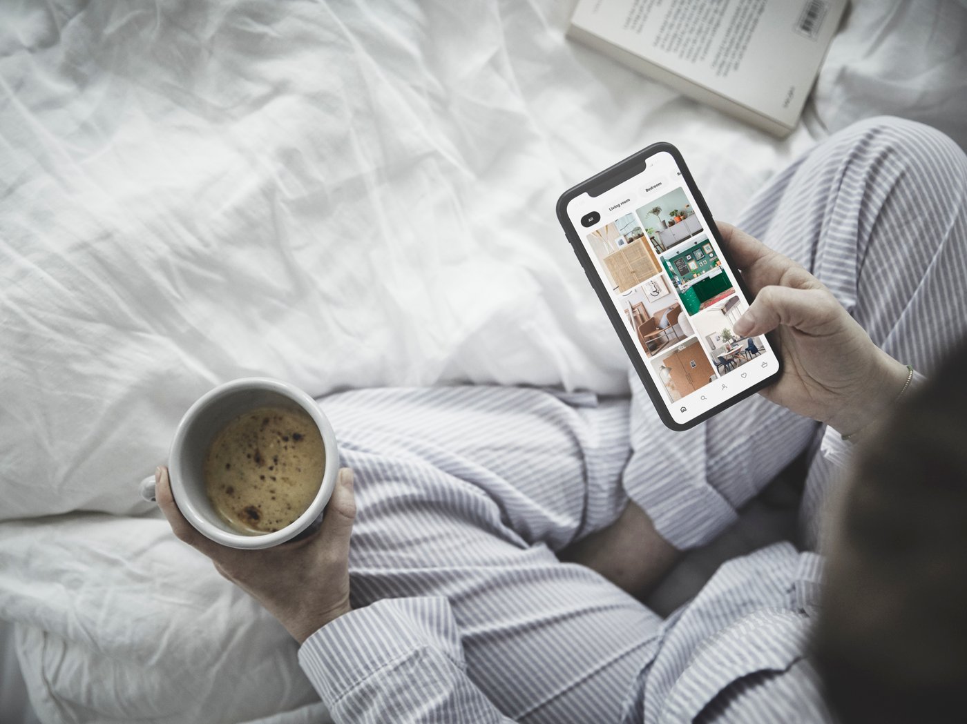 Ženska na postelji, v rokah drži telefon in kavo