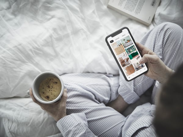 Mujer con café y móvil buscando productos IKEA encima de su cama