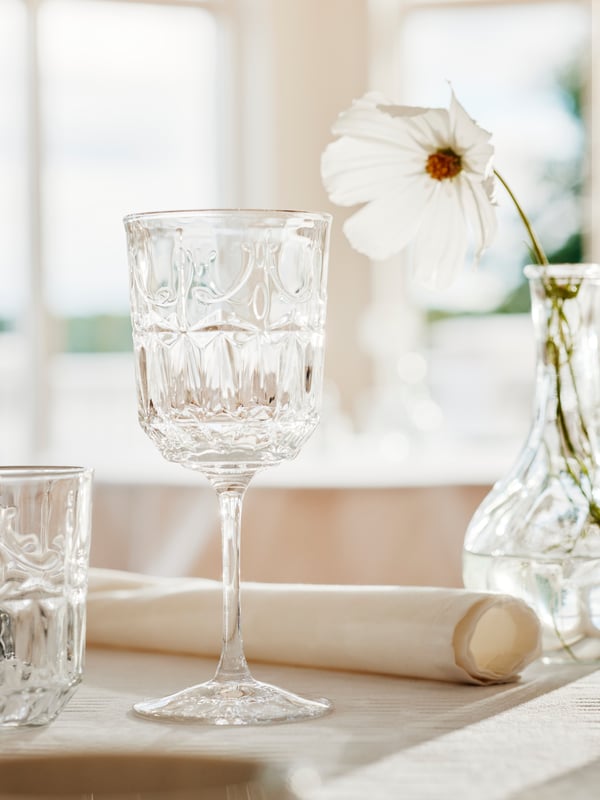 2 SÄLLSKAPLIG glas på et flot dækket bord i romantisk stil med en VILJESTARK vase med en hvid blomst i i baggrunden.