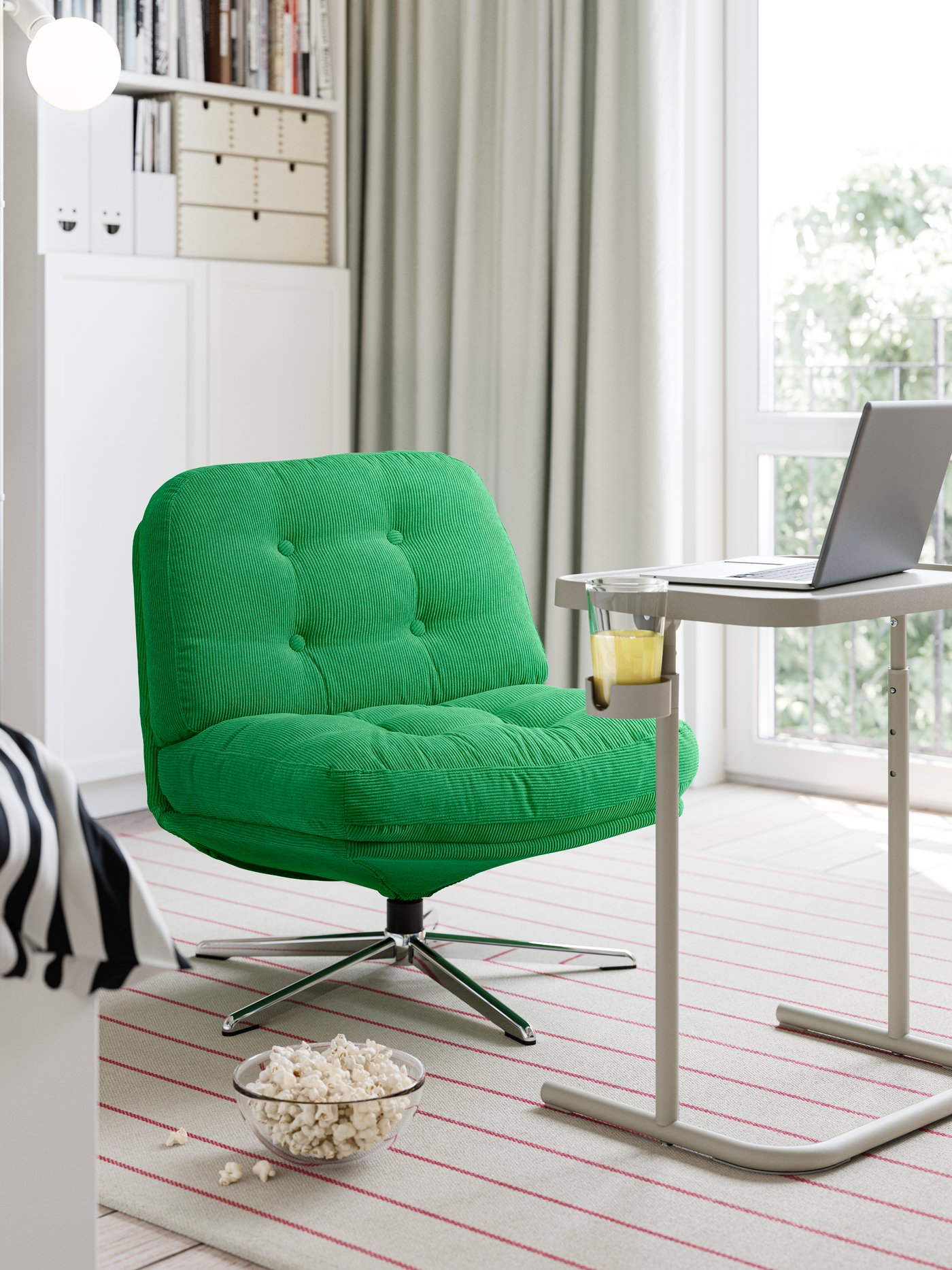 An armchair with a BJÖRKÅSEN laptop stand in grey in front of it, with a cup of juice in the holder.