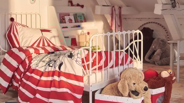 Letto allungabile MINNEN turchese nell’angolo di una cameretta, con giocattoli, lampada da lettura e mobili.