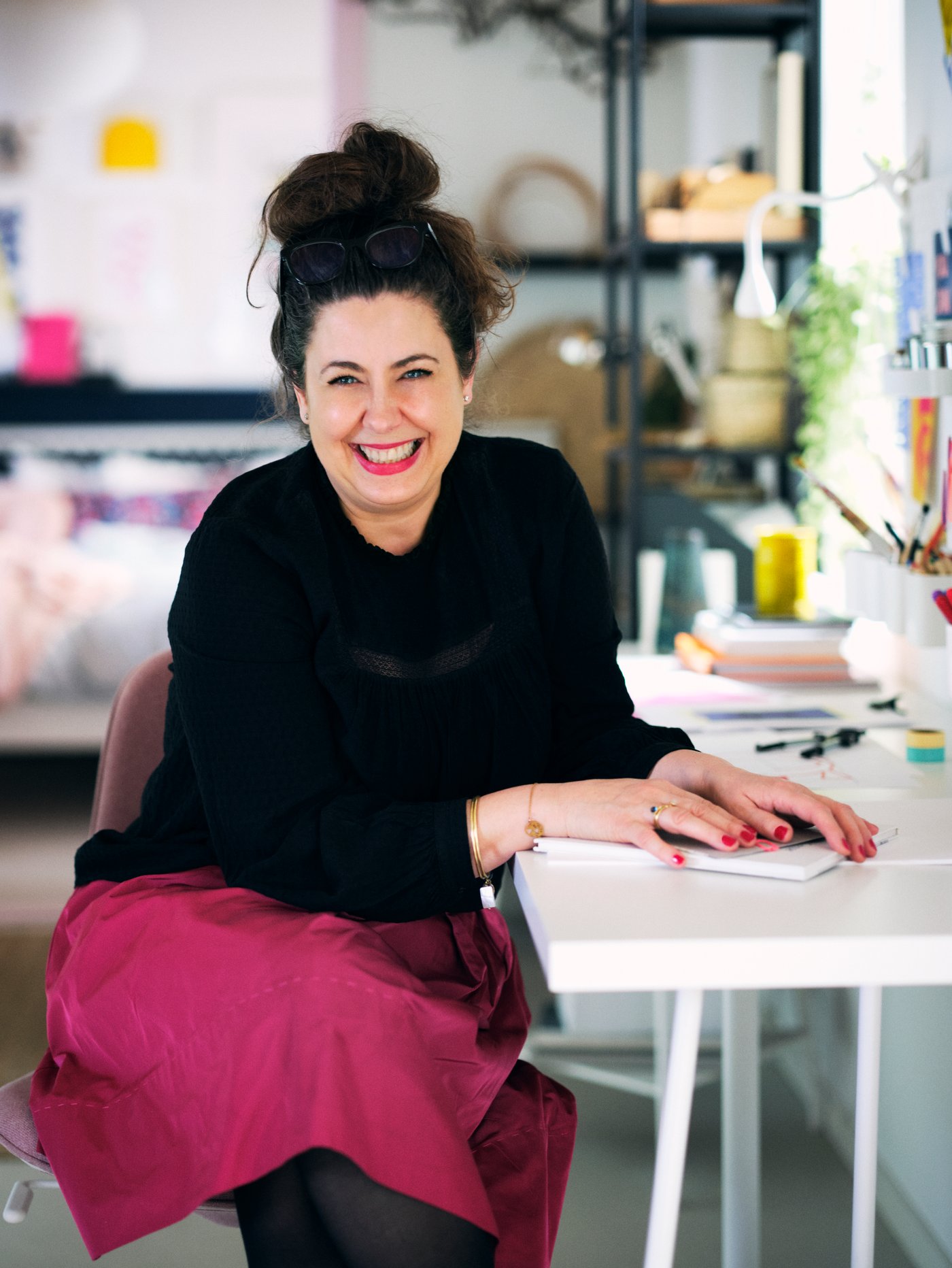 A woman sitting at a white LAGKAPTEN/TILLSLAG table with a white NÄVLINGE clamp spotlight and anthracite ENHET shelving unit.