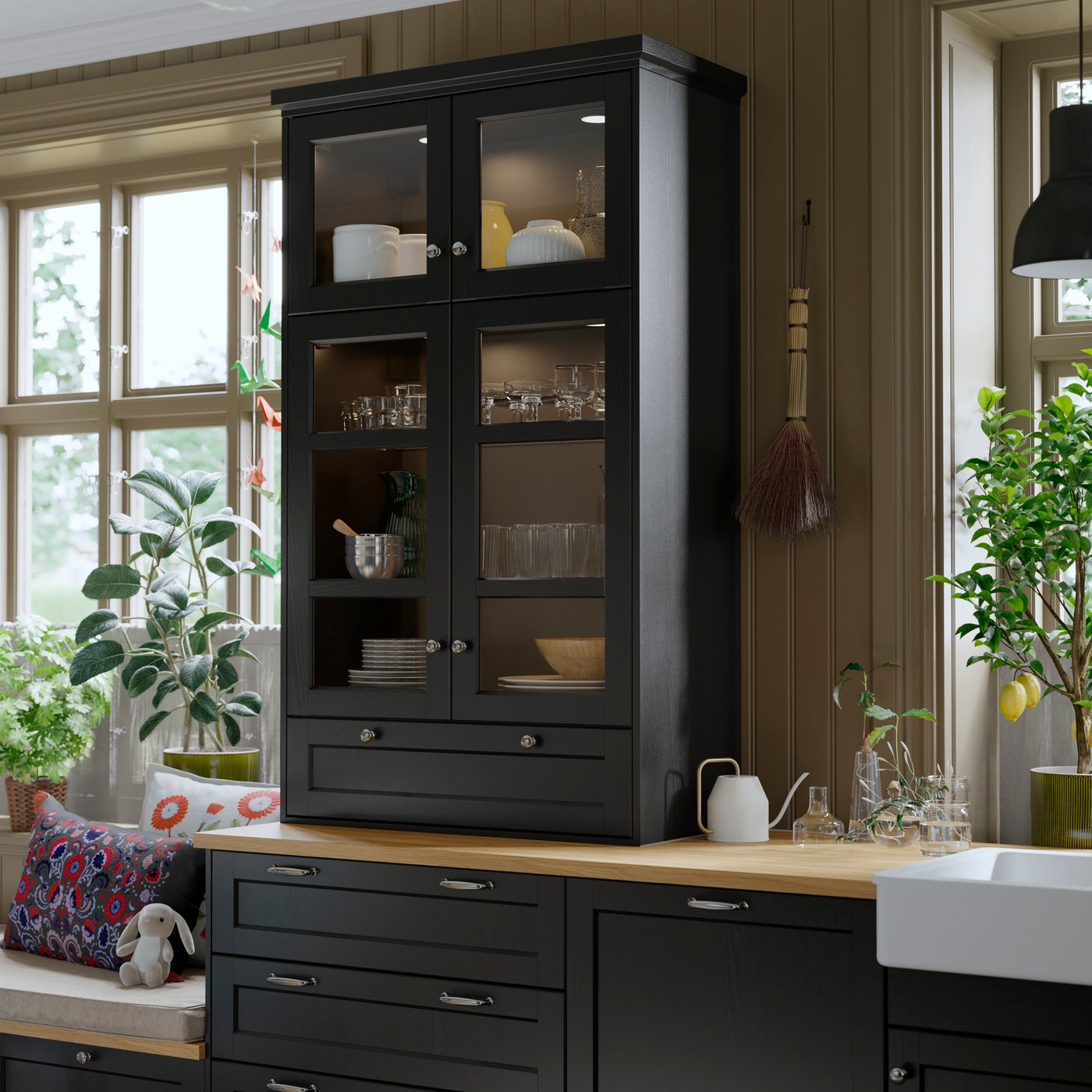 A kitchen with a black stained LERHYTTAN glass door cabinet displaying glassware and tableware, against wooden walls