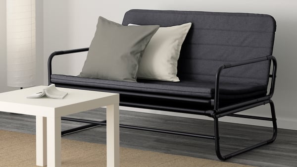 Svart HAMMARN bäddsoffa med metallram och enkla kuddar vid ett litet soffbord.
