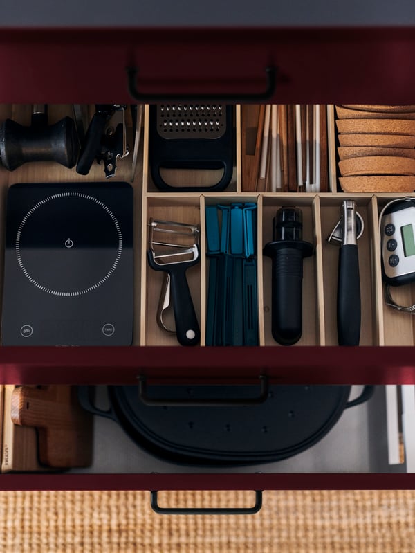 An open kitchen drawer with red-brown KALLARP front, showing an UPPDATERA cutlery tray inside holding various utensils.