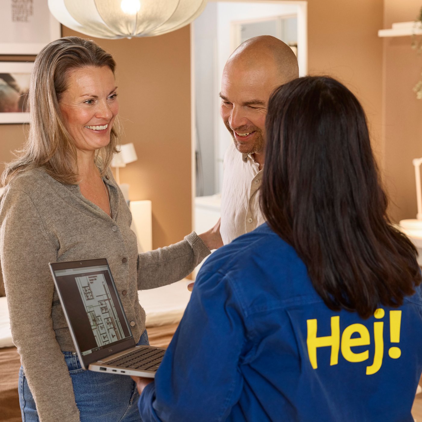 IKEA co-worker sat at her desk beside a wall of windows, talking to a customer through a headset whilst on her computer and taking hand notes 