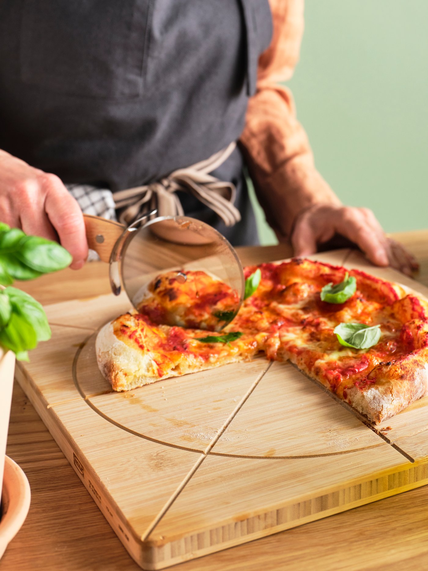 Une personne coupant une pizza avec un rouleau à découper, sur une planche en bois.