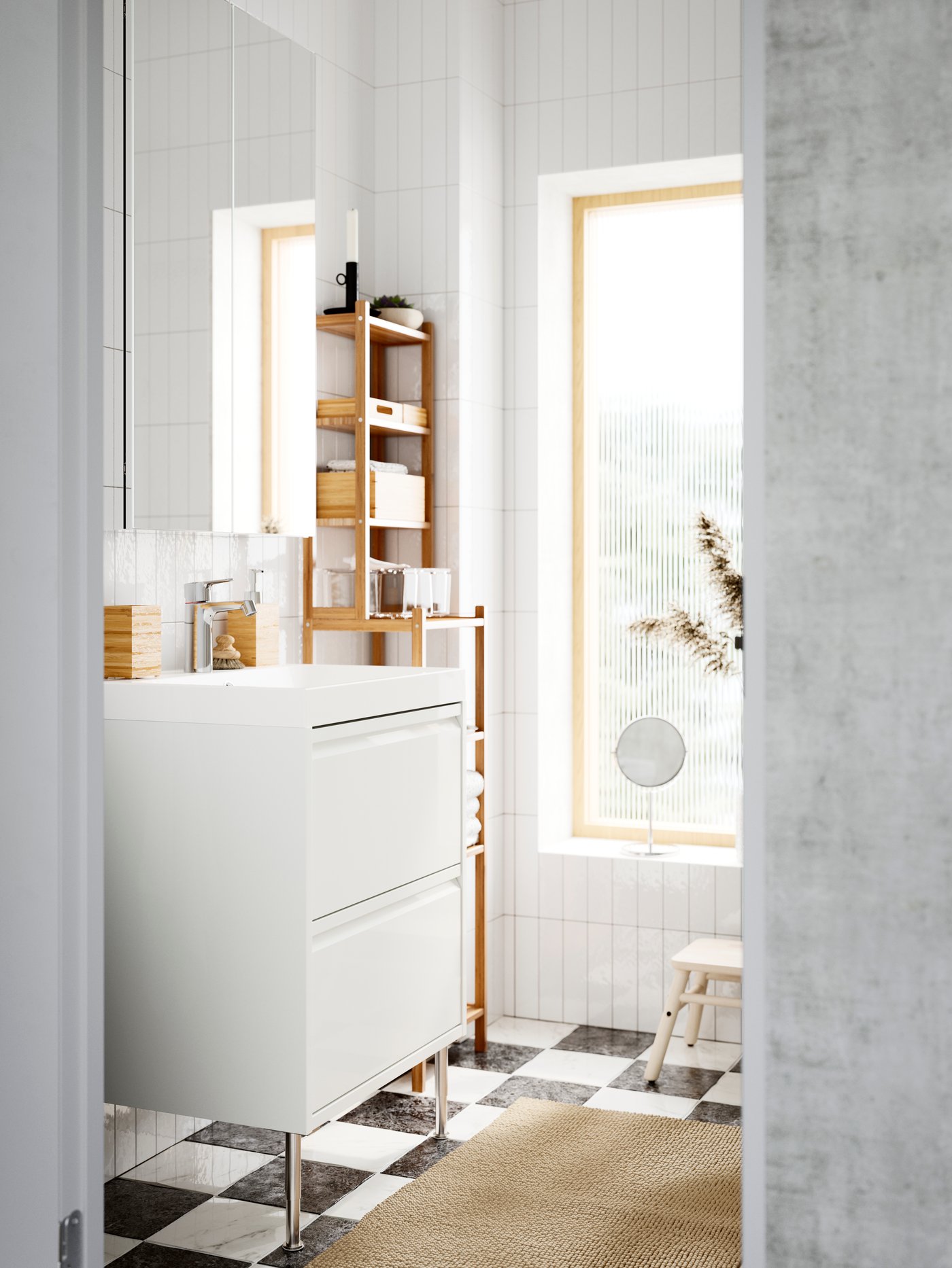 Ett ljust badrum med vita kaklade väggar har ett högblankt vitt ÄNGSJÖN tvättställ med integrerade handtag vid bambuhyllor.