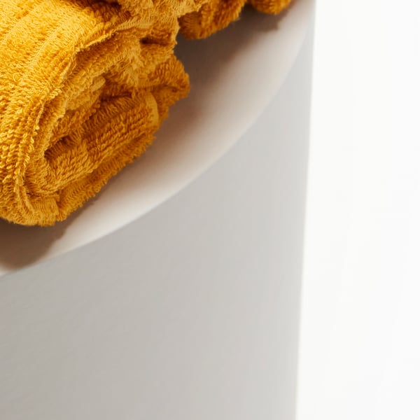 A closeup of two tightly rolled-up yellow VÅGSJÖN towels, placed on a white surface.