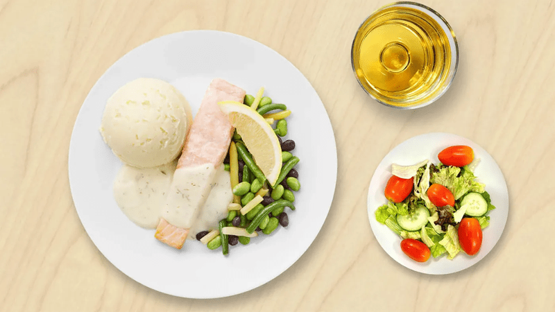 Puutaustaa vasten on lohifilee lautasella, pieni salaatti omalla lautasella ja juomalasissa juoma.