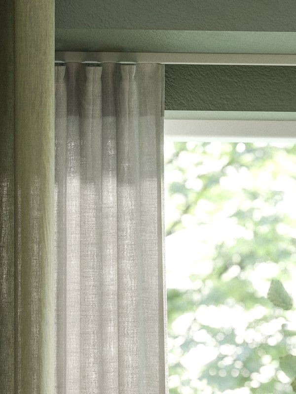 Gröna och naturvita linnegardiner hängande i förnster med grönskande träd utanför. 