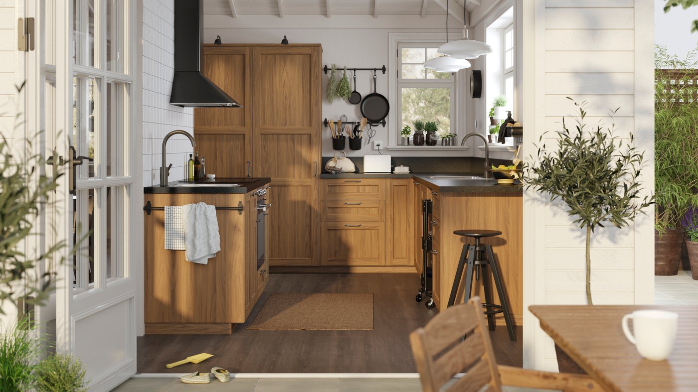 Une cuisine blanche de style traditionnel baignée de soleil avec des façades ENKÖPING à motif noyer brun et des plans de travail à motif minéral noir.