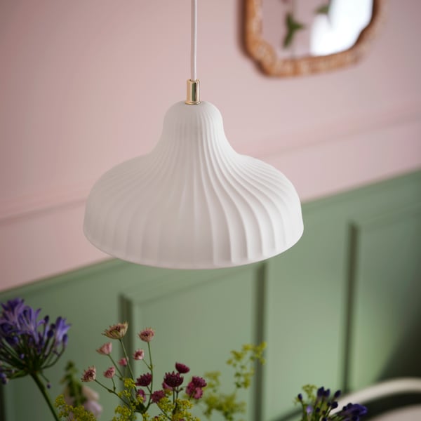 An off-white SKIVTOFS pendant lamp with a ribbed texture hangs against a pink and green wall, adding elegance to the room.