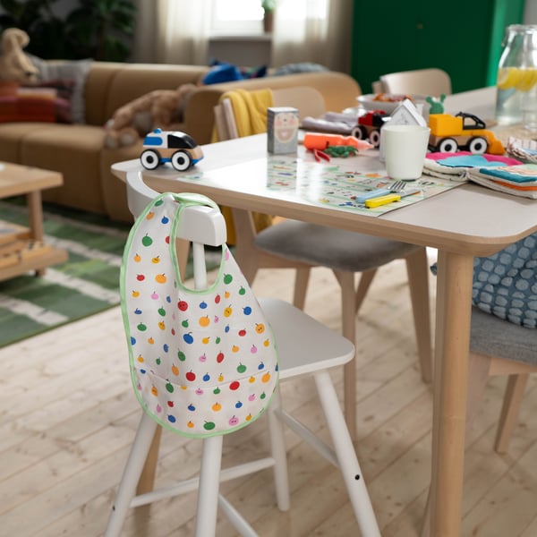 Un seggiolone bianco per bambini con un bavaglino decorato con frutta colorata appeso allo schienale.